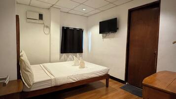 A hotel room with a single bed, a wooden table, a TV mounted on the wall, and a door.