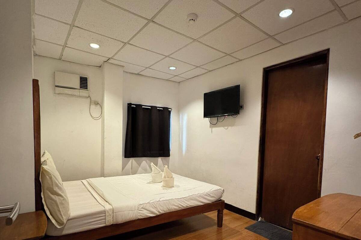 A hotel room with a single bed, a wooden table, a TV mounted on the wall, and a door.