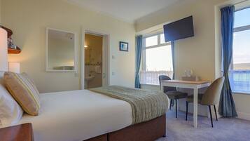A bedroom with a bed, a desk, a chair, a TV, and a window with curtains.