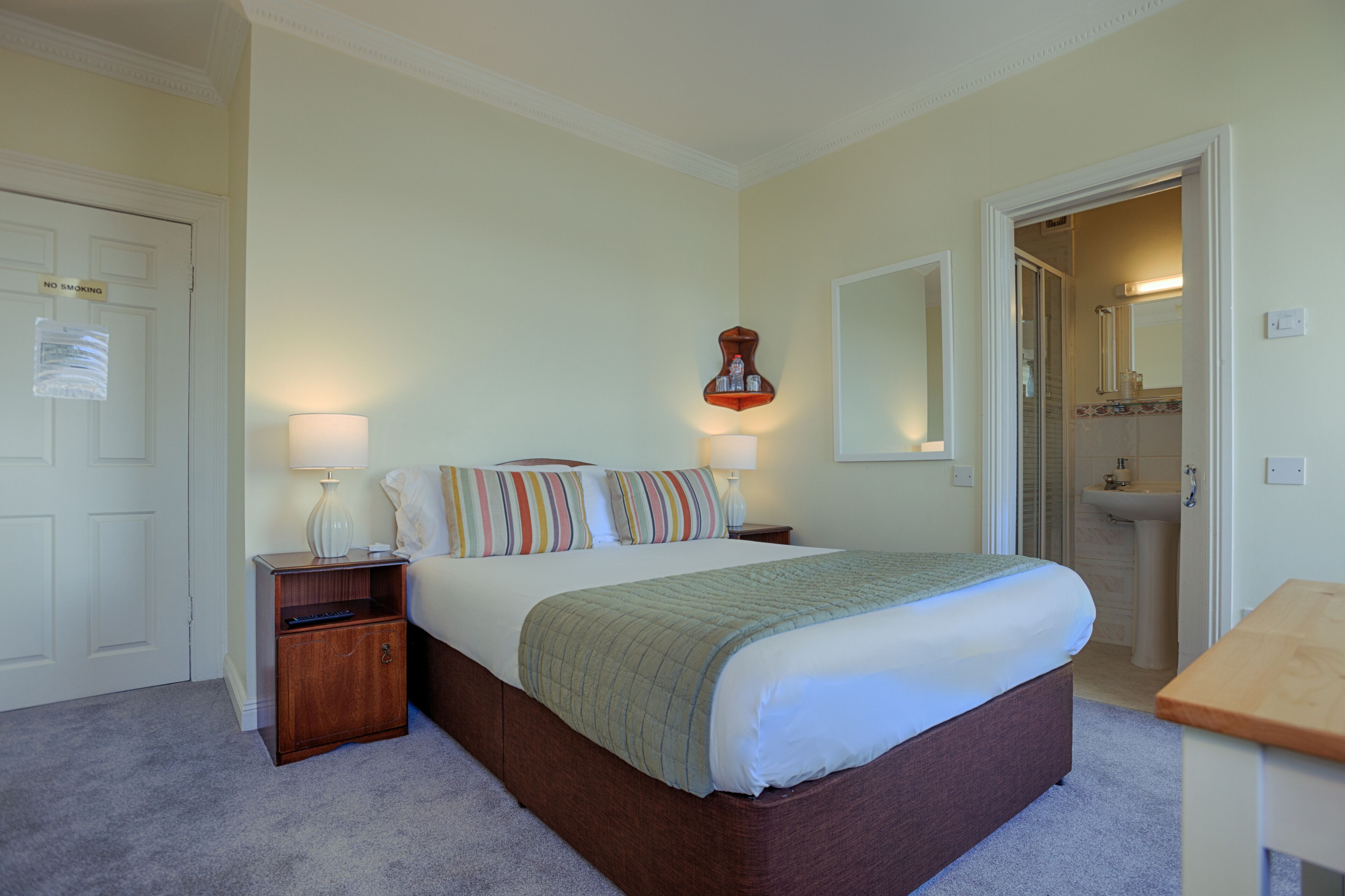 Un dormitorio ordenado con cama, lámparas de noche, una mesita de noche y un banco de madera.