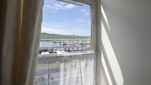 A view through a window with a curtain, revealing a marina with boats and a distant hilly landscape. - The Waterfront (Dingle)