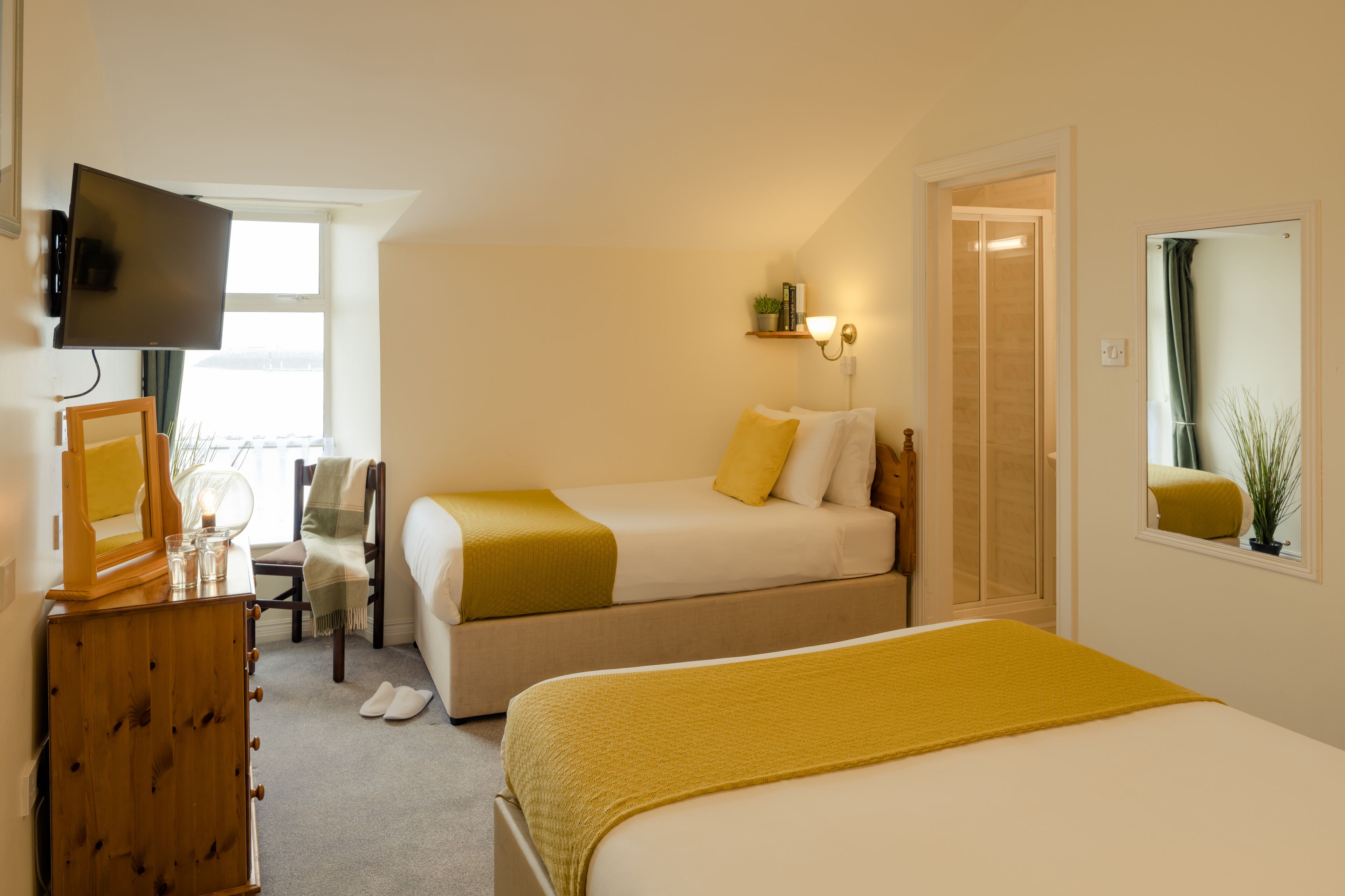 A hotel room with two beds, a TV, a desk with a chair, a mirror, and a window.