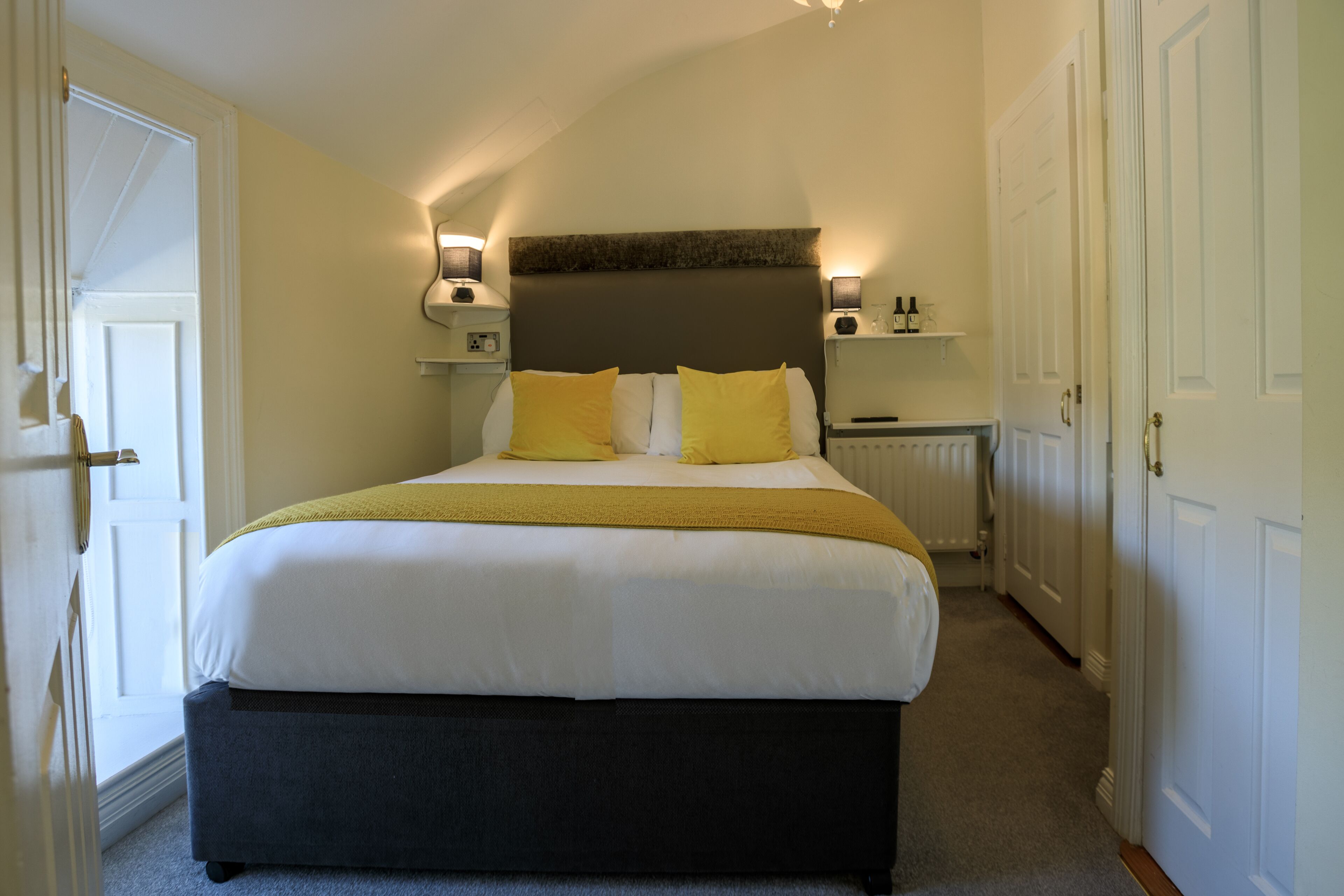 A neatly made bed with white and yellow bedding, a dark headboard, and bedside lamps.