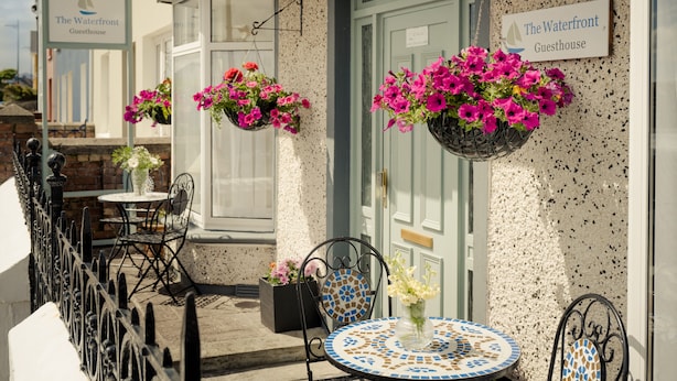 A guesthouse with hanging flower baskets, outdoor seating, and a tiled table. - The Waterfront (Dingle)