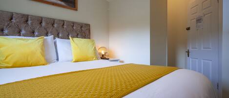 A neatly made bed with a yellow blanket and pillows, a tufted headboard, and a painting on the wall.