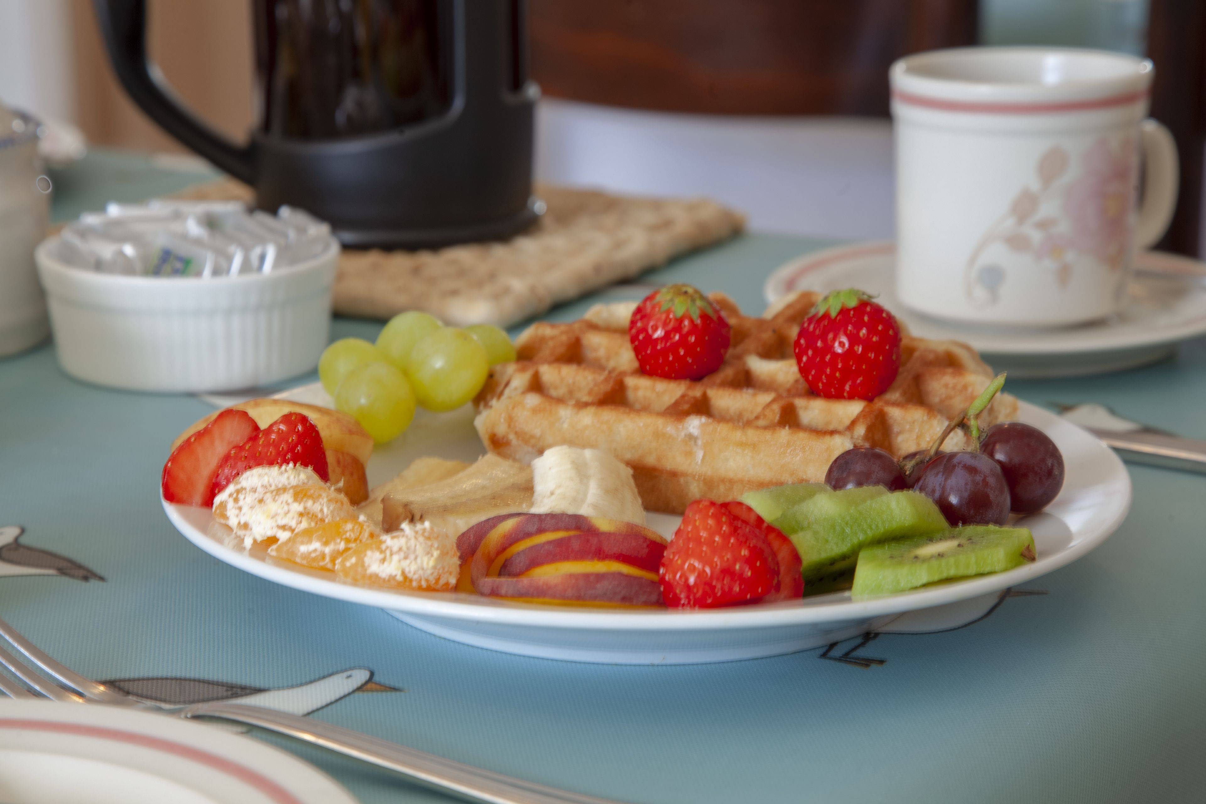 Un plato de desayuno con waffles, fresas, uvas, kiwi y rodajas de melocotón.