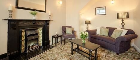 A living room with a fireplace, two armchairs, a sofa, a coffee table, and patterned carpet.