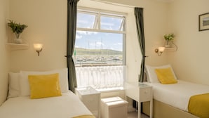 A hotel room with two beds, a desk, and a window with a view of boats. - The Waterfront (Dingle)