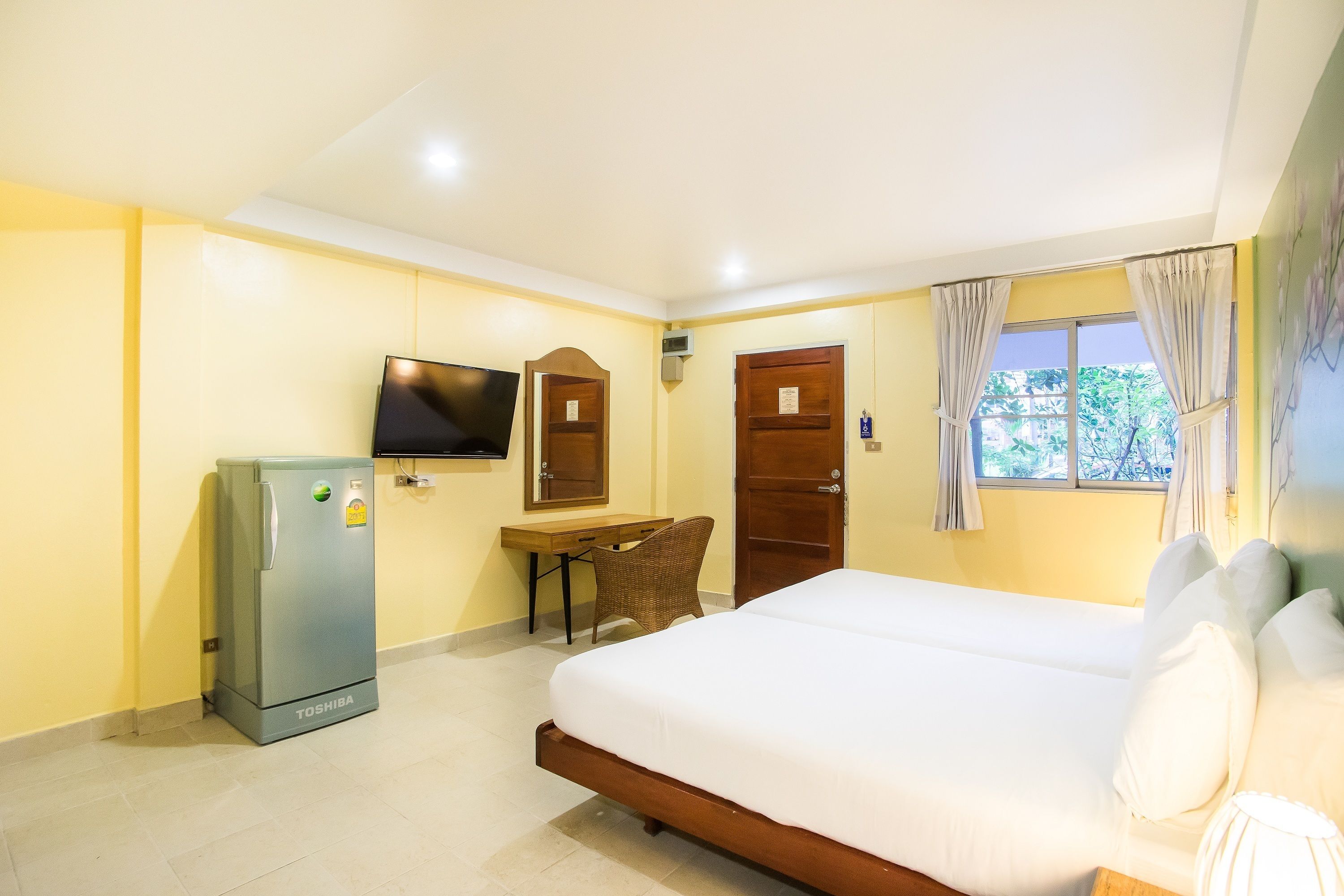 A hotel room with a bed, a desk, a refrigerator, a television, and a window with curtains.