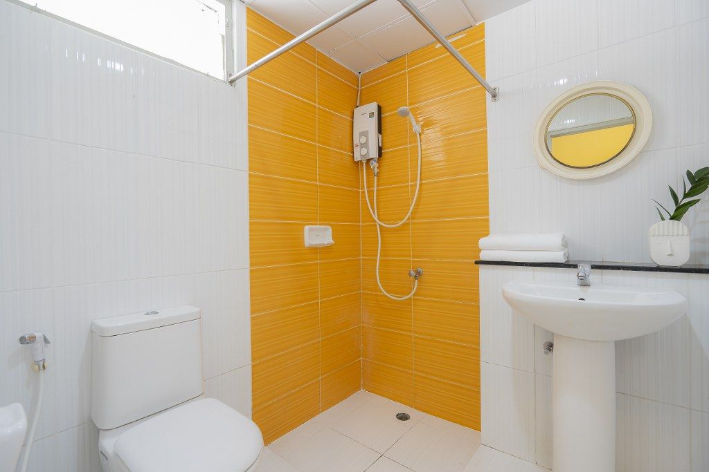 Un baño con inodoro blanco, ducha con pared amarilla, lavamanos y espejo.
