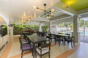 An outdoor dining area with multiple tables and chairs, a ceiling fan, and a view of a pool. - Sawasdee Place Hotel (Pattaya)