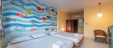 Habitació d'hotel amb tres llits, un mural de peixos a la paret, una cadira de vimet i un frigorífic.