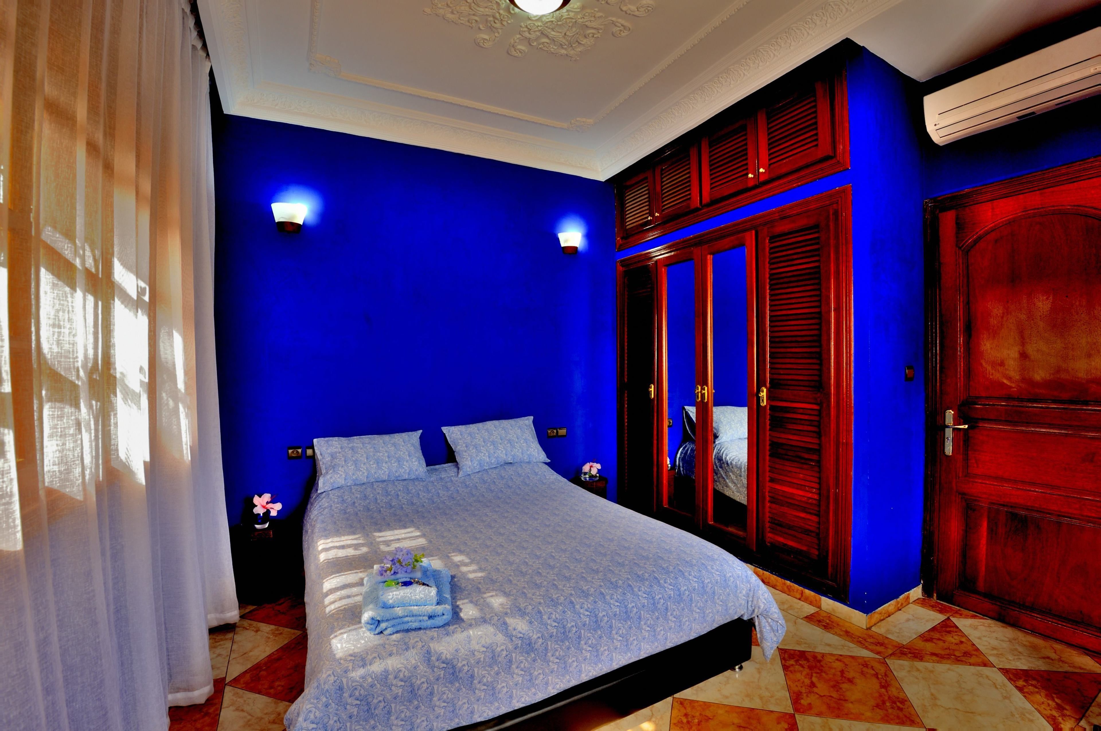 A bedroom with a blue wall, a bed with a white bedspread, two bedside lamps, and a wooden wardrobe.
