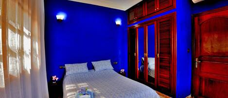 A bedroom with a blue wall, a bed with a white bedspread, two bedside lamps, and a wooden wardrobe.