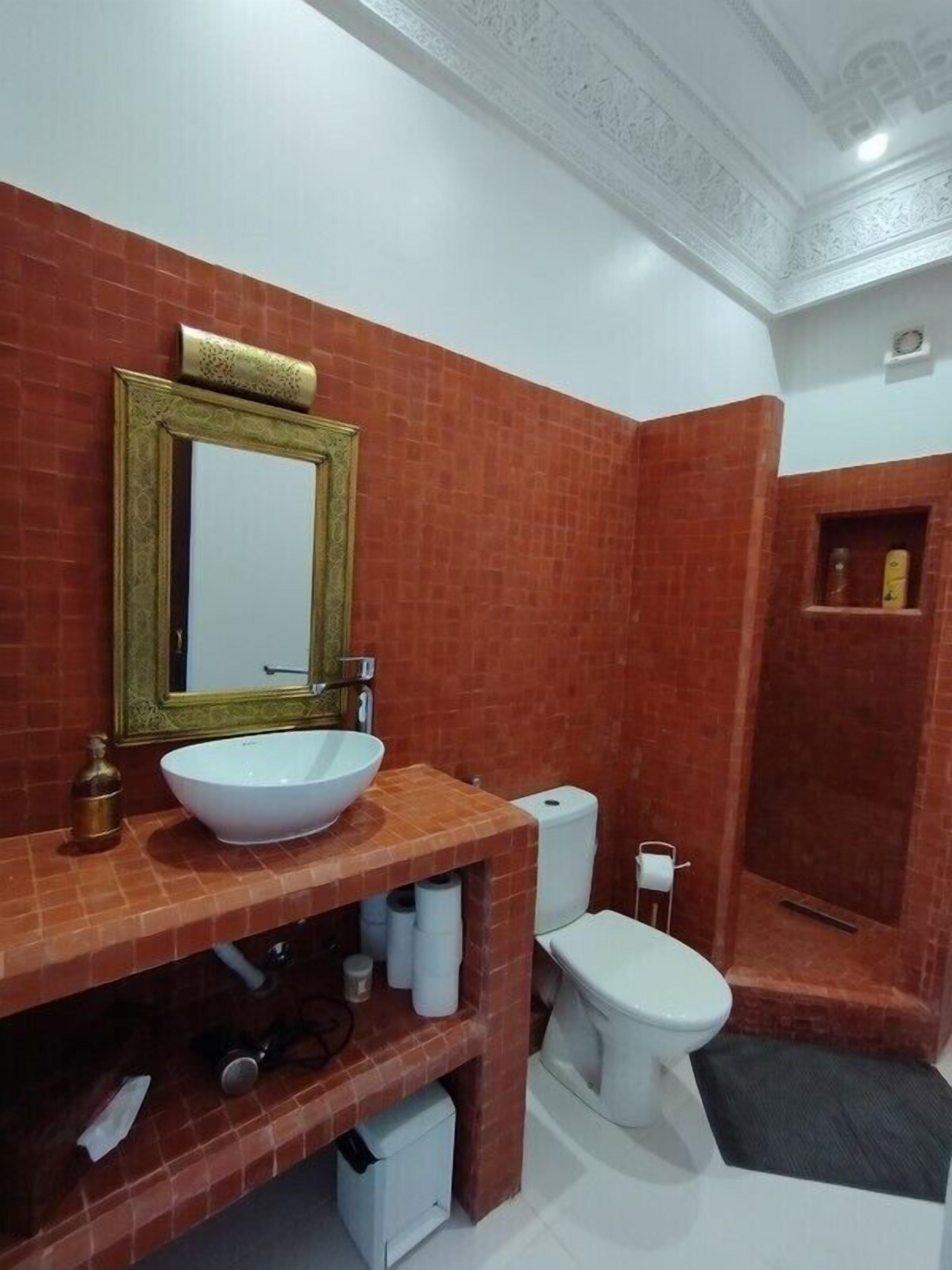 Een badkamer met een grote witte wastafel, een spiegel met gouden lijst, een toilet en een douchehoek.