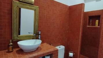 Een badkamer met een grote witte wastafel, een spiegel met gouden lijst, een toilet en een douchehoek.