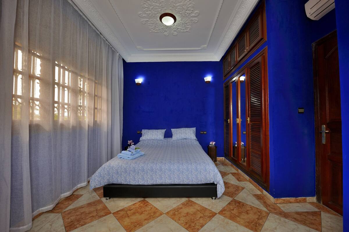 Une chambre à coucher avec un lit, des rideaux, une table de chevet et un climatiseur fixé au mur.