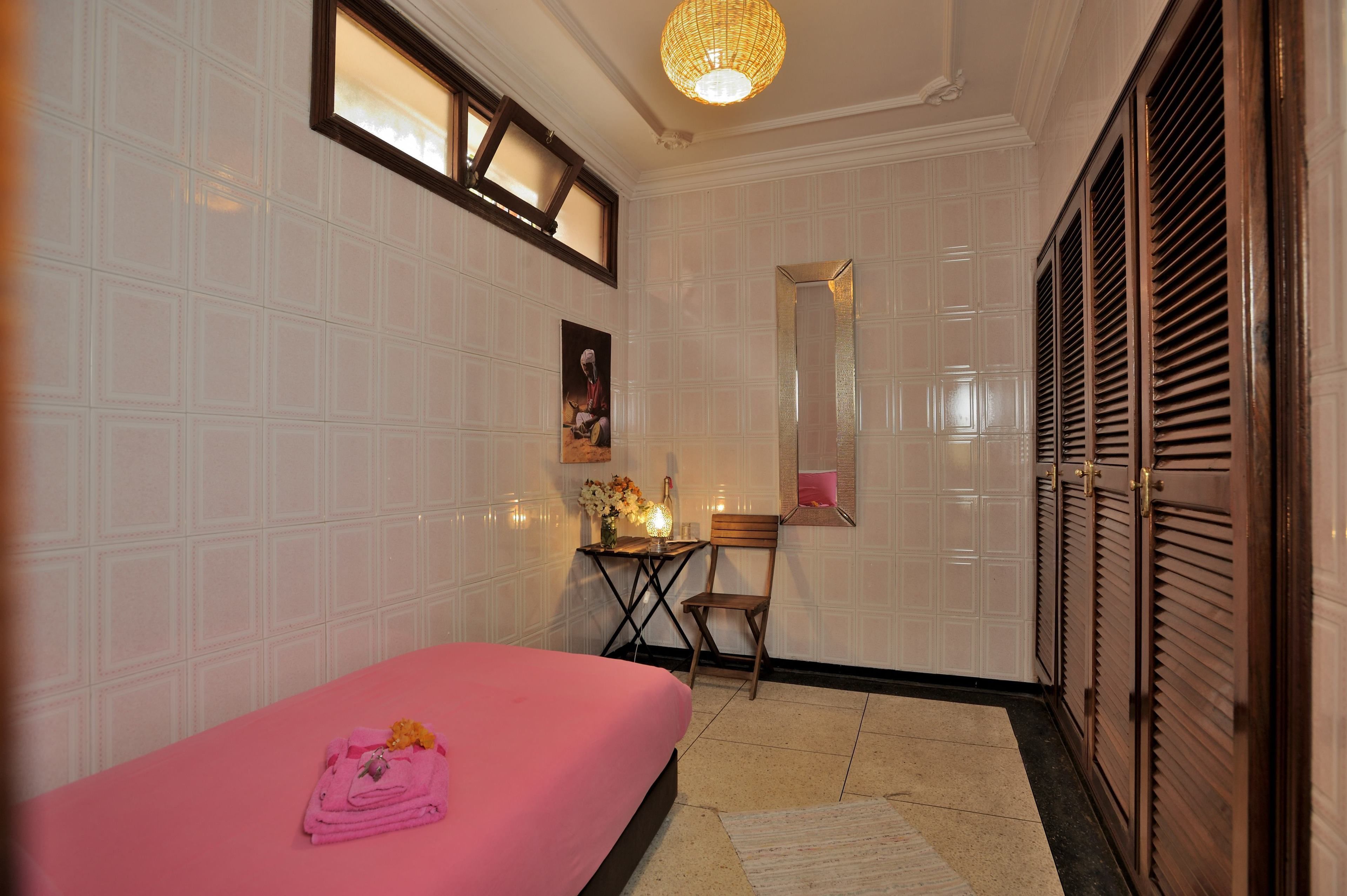 A room with a bed, a chair, a table with flowers, a mirror, and a wardrobe.