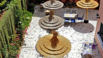 A courtyard with a central table and chairs, surrounded by decorative umbrellas and lush greenery.