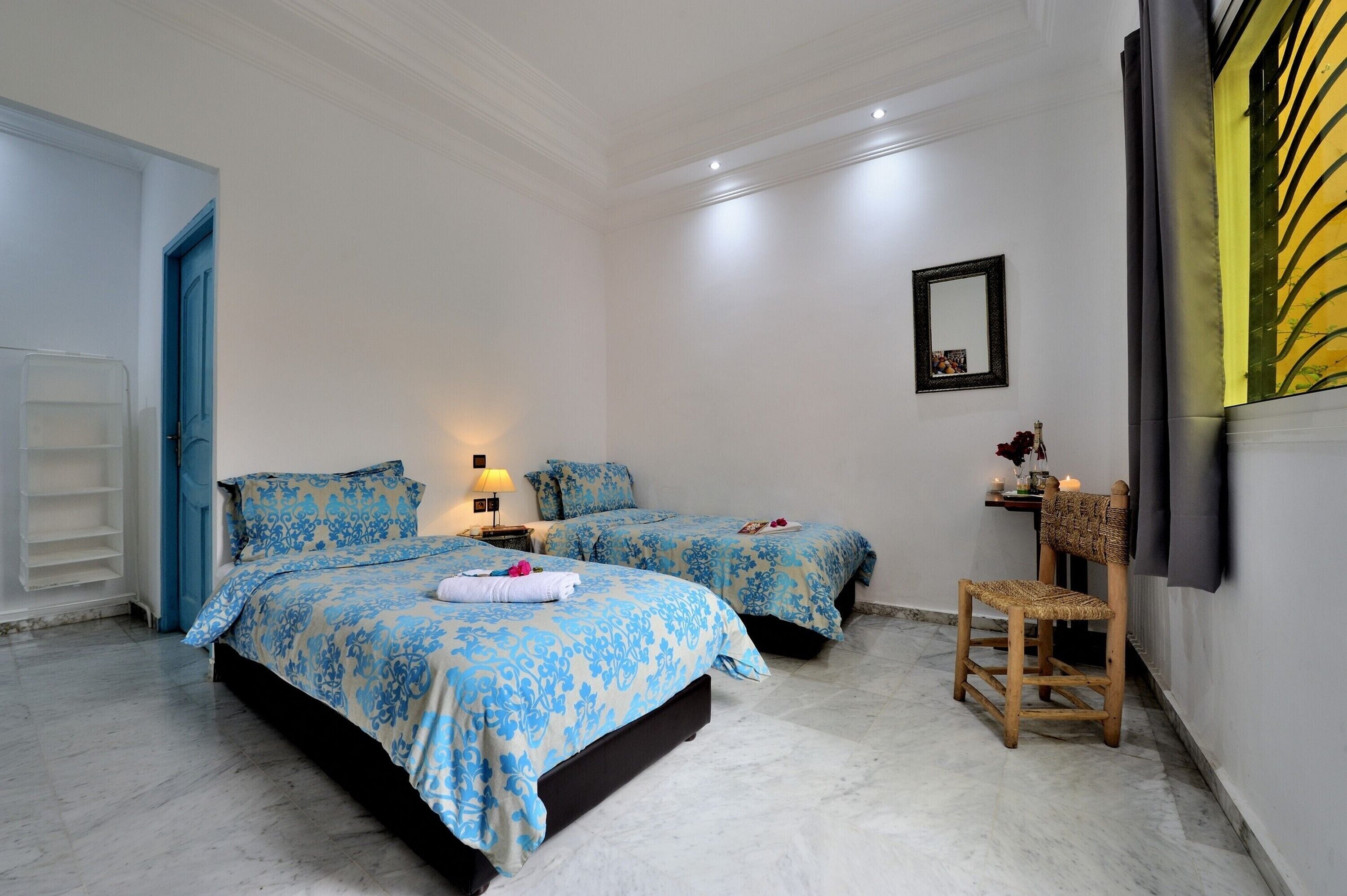Un dormitorio con dos camas, una silla de madera, una mesita con una lámpara y un espejo en la pared.