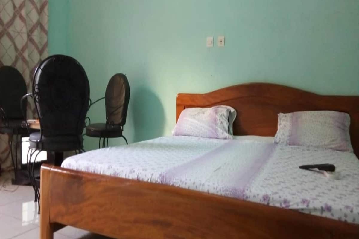 A single-bed room with a wooden headboard, a desk with a chair, and a patterned bedspread.