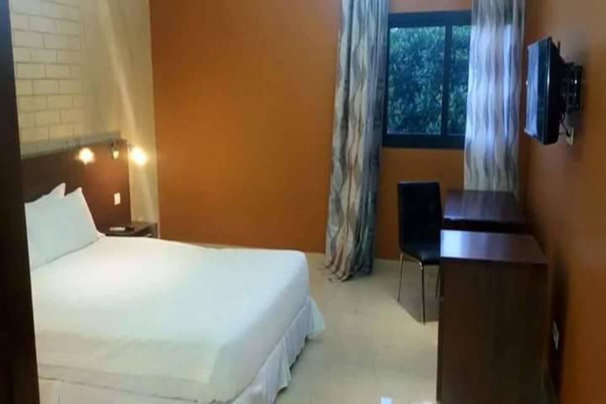 A hotel room with a bed, a desk, a chair, and a TV.