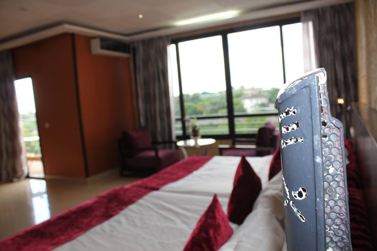 A hotel room with a large bed, a view of the outdoors through the window, and a small round table in the corner.