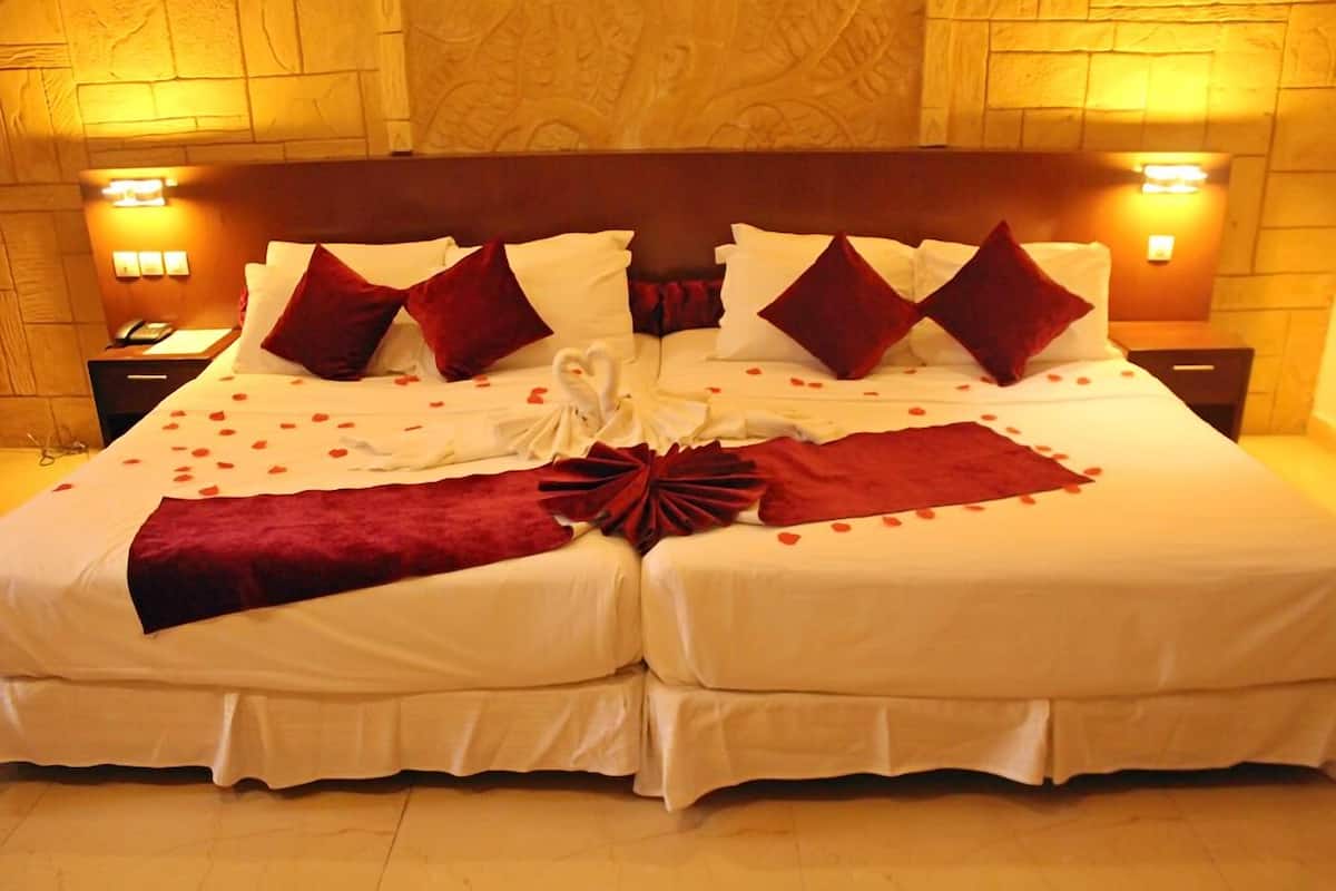 A double bed with white linens, red pillows, and a heart-shaped decoration on the bedspread.