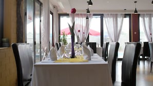 Een restaurant met een lange eettafel, voorzien van zwarte leren stoelen en een witte tafelkleed.
