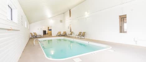An indoor swimming pool with clear water, surrounded by white walls and a high ceiling.