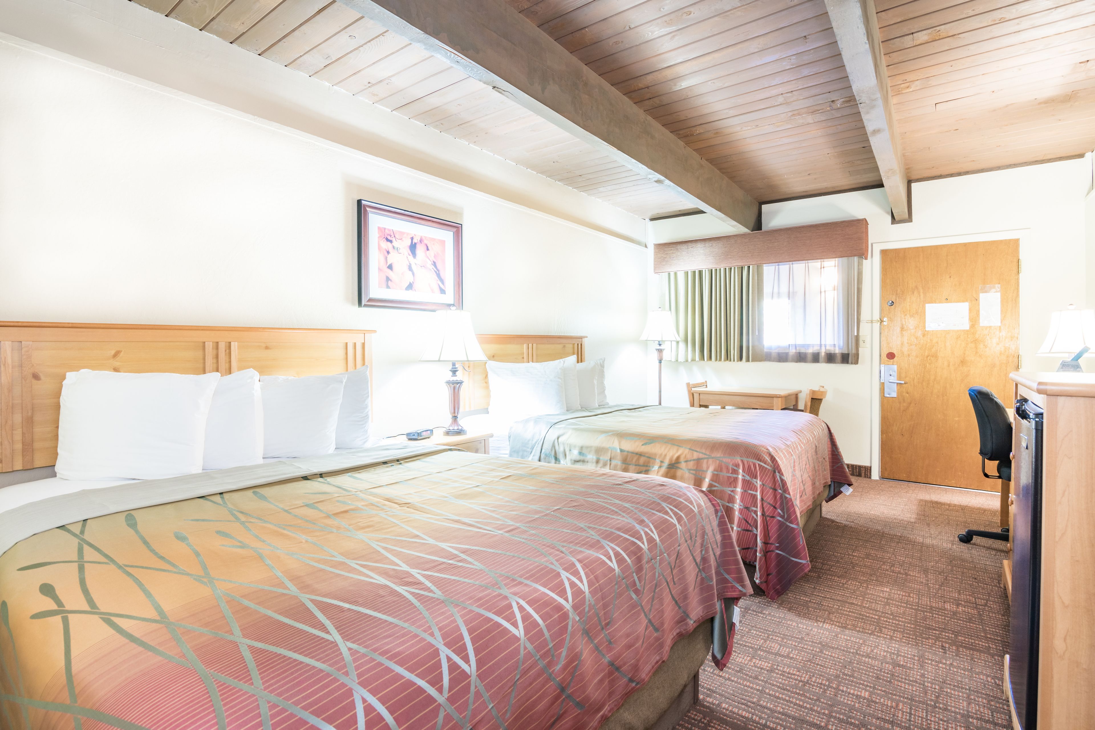 Una habitación de hotel con dos camas, techo de madera, escritorio y puerta.