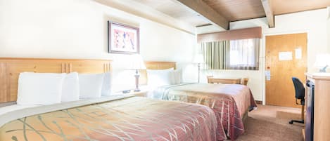 Una habitación de hotel con dos camas, techo de madera, escritorio y puerta.