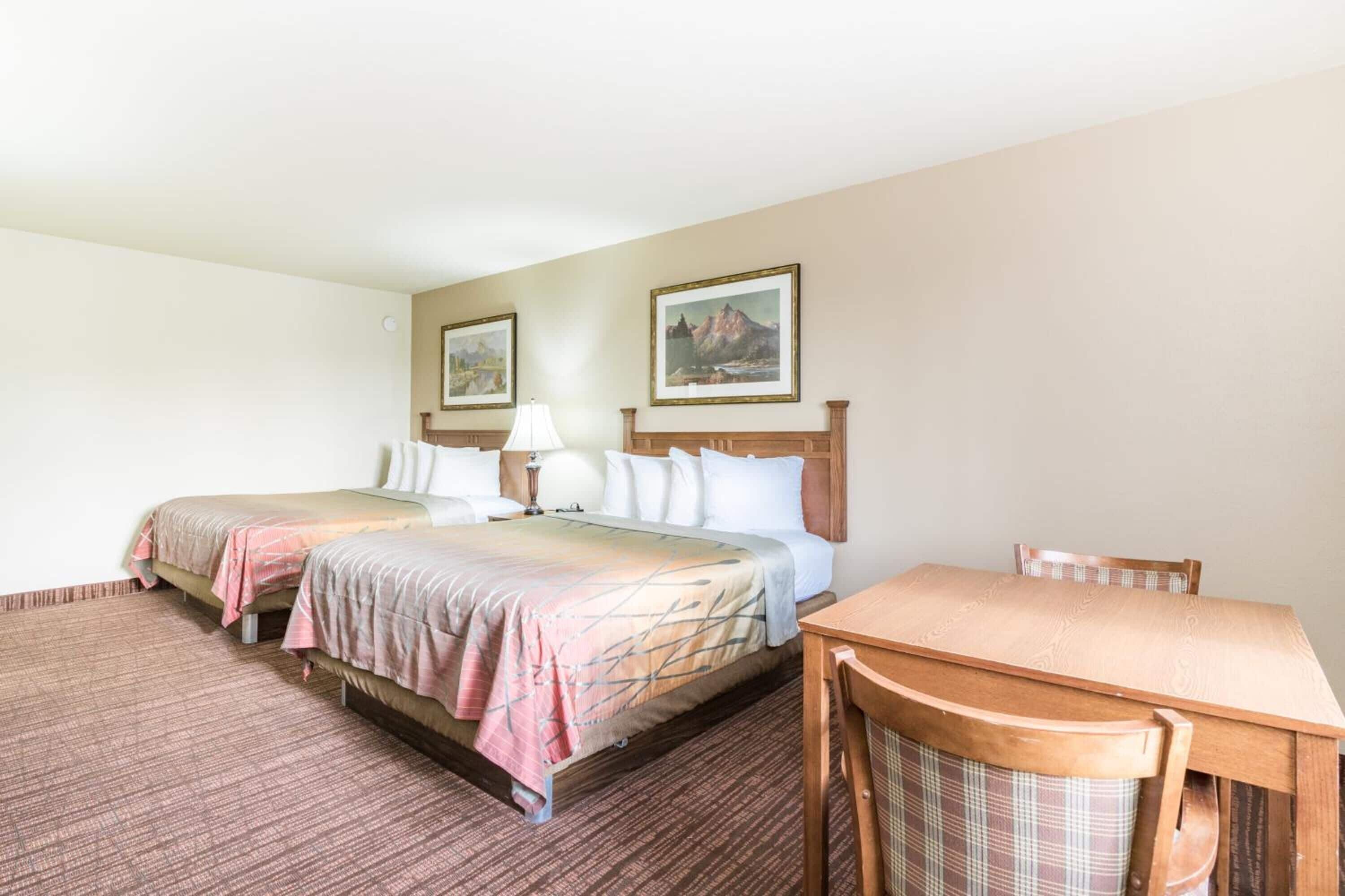 Een hotelkamer met twee bedden, een houten tafel en een stoel.
