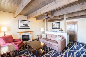 A cozy living room with a fireplace, a red armchair, a patterned rug, and a ceiling fan. - Teton West Motel (Driggs)