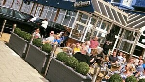 A group of people seated at outdoor tables in front of a building with a blue facade and a sign that reads "Welcome". - Lyndene Hotel (Blackpool)
