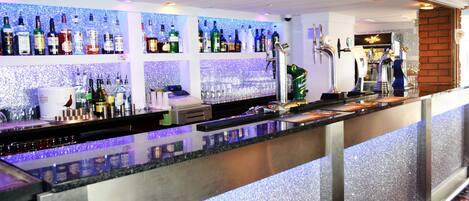 Un espace bar avec des étagères remplies de bouteilles d’alcool, une caisse enregistreuse et un robinet à bière.