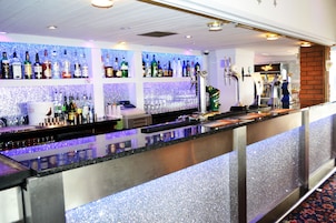 Een bar met flessen drank op de planken, een kassa en een biertap.