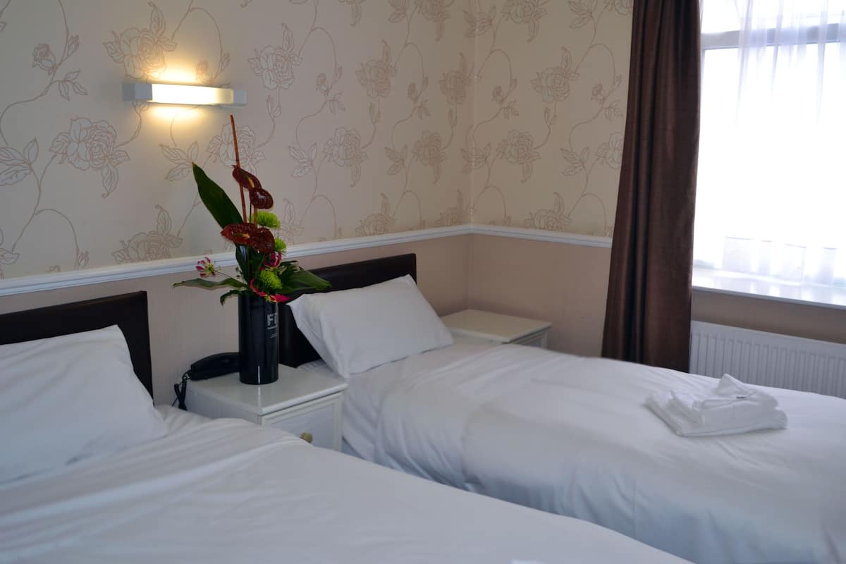 A hotel room with two beds, a nightstand with a lamp, and a floral wallpaper.