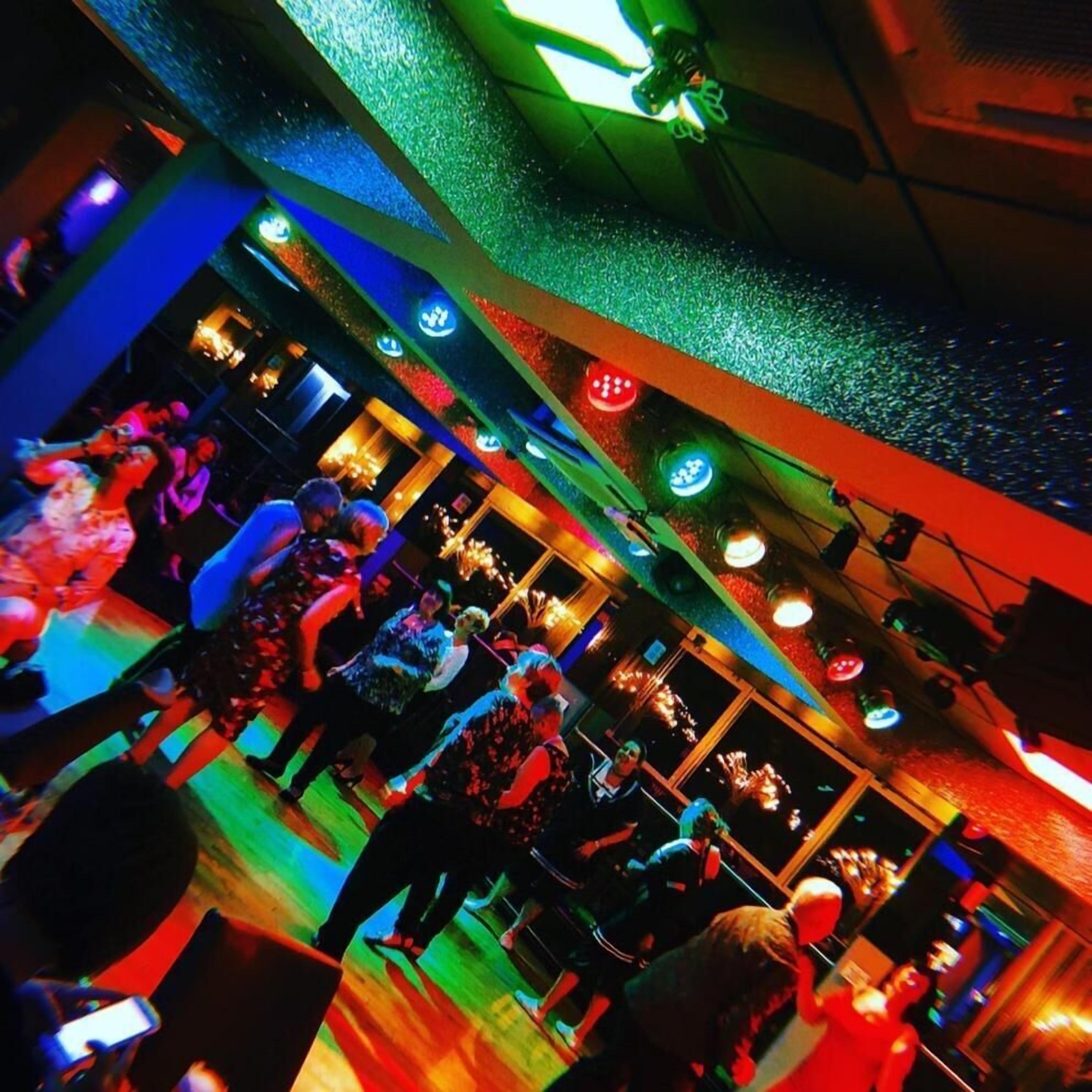 A crowded indoor space with people dancing, illuminated by colorful lights.