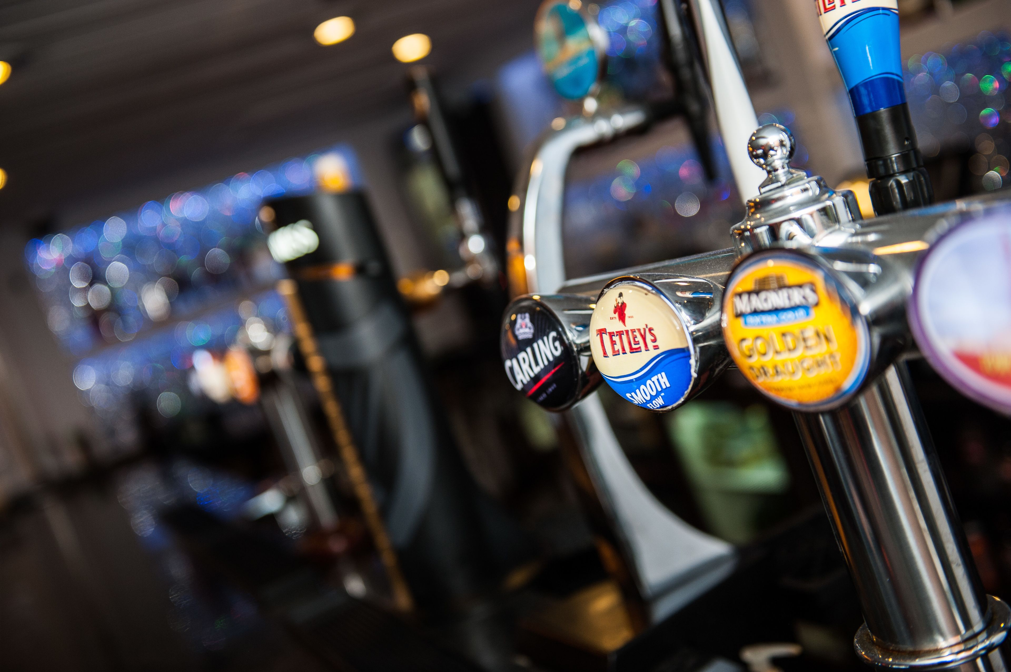 Primer plano de grifos de cerveza con etiquetas como 'Carling', 'Teller' y 'Magners'.