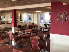 Een restaurantgedeelte in een hotel, met gestreepte stoelen, gedekte tafels en een decoratief kunstwerk aan de muur.