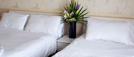 Habitación de hotel con dos camas, ropa de cama blanca, un florero con flores y un diseño de papel tapiz floral.
