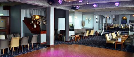 A hotel lobby with a wooden floor, seating areas, and a staircase.