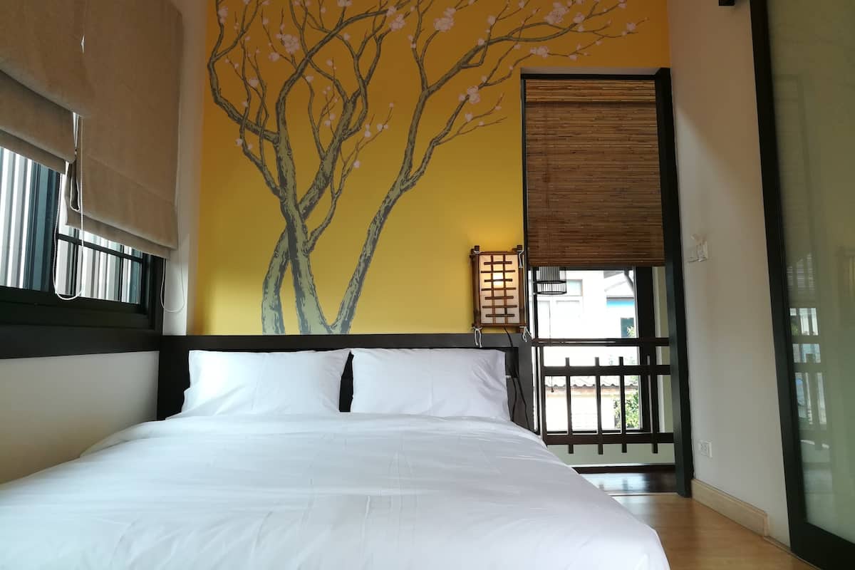 A bedroom with a bed, a window with a view, a wall with a tree mural, and a wooden headboard.