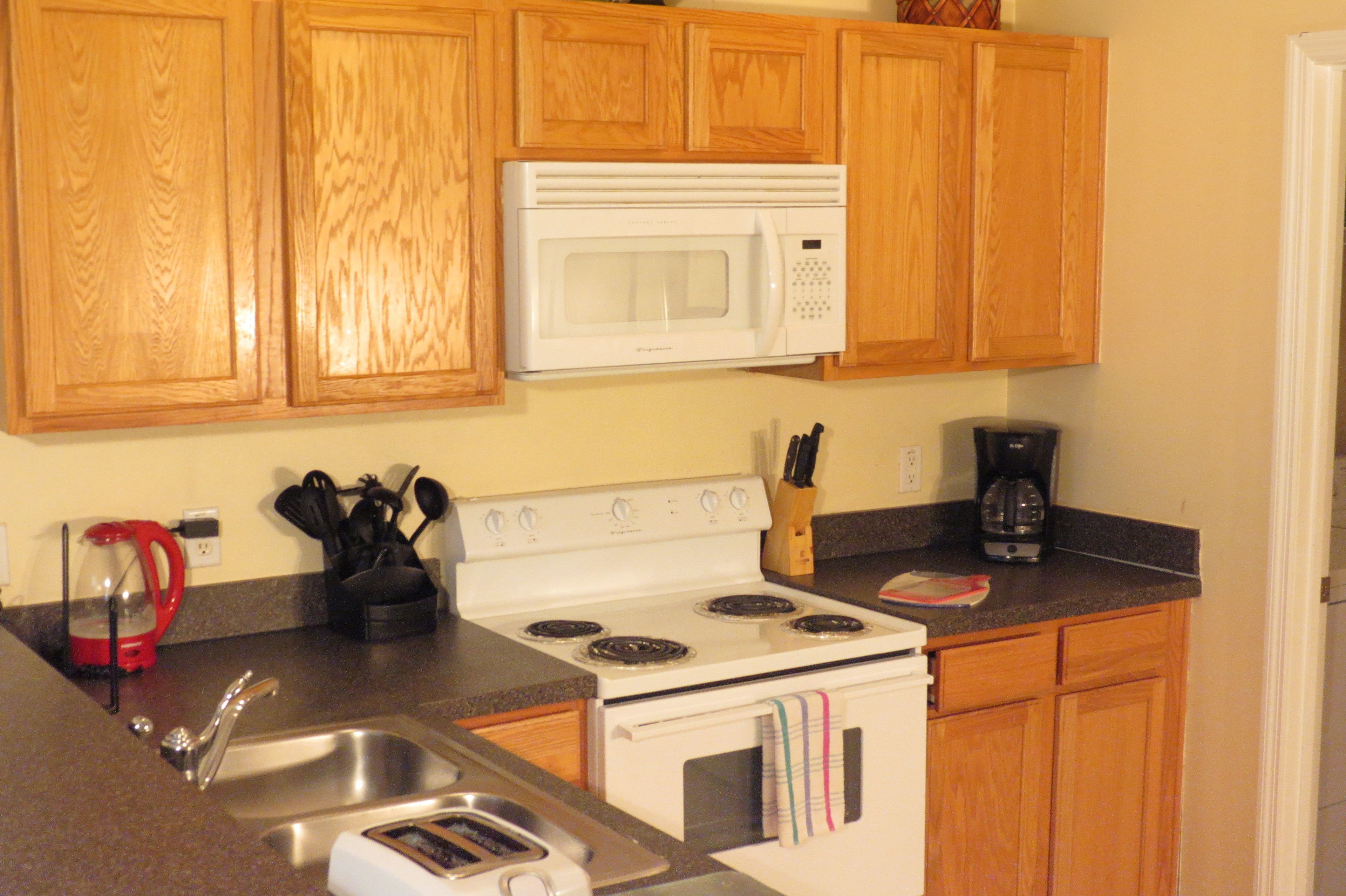 A kitchen with wooden cabinets, a white microwave, a stove, a sink, and a coffee maker.