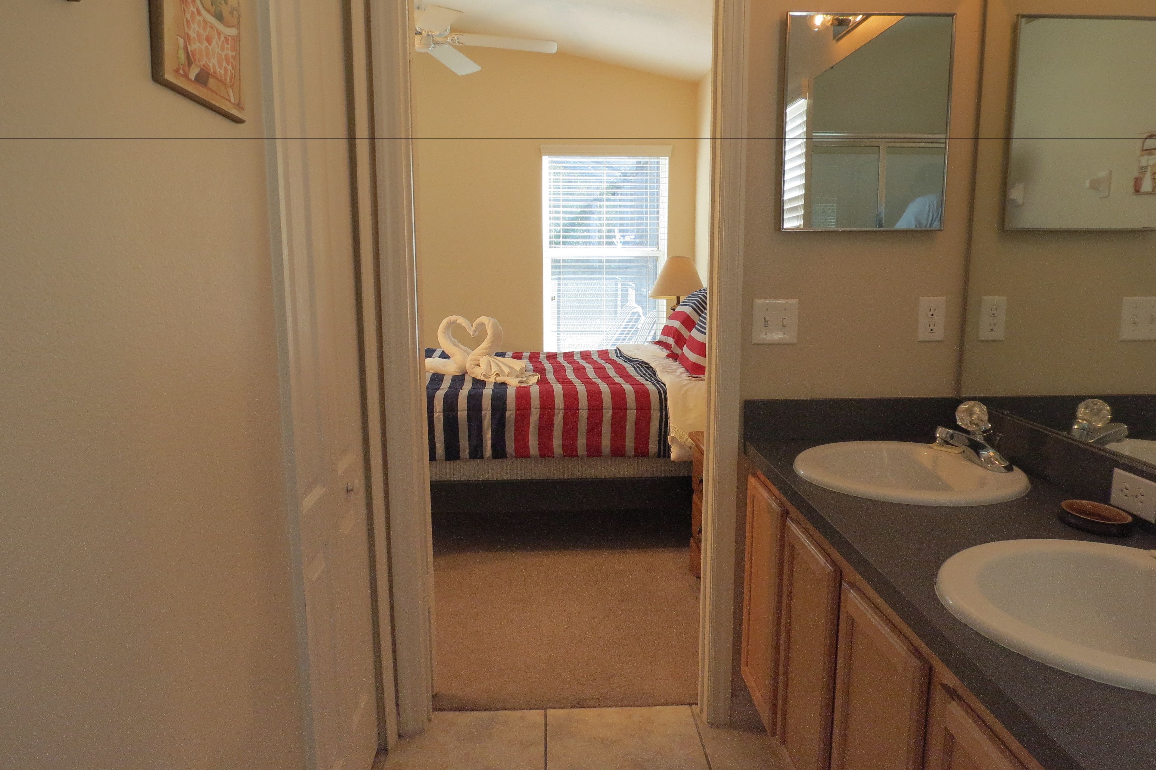 A bedroom with a bed, a window, and a bathroom with two sinks and a mirror.