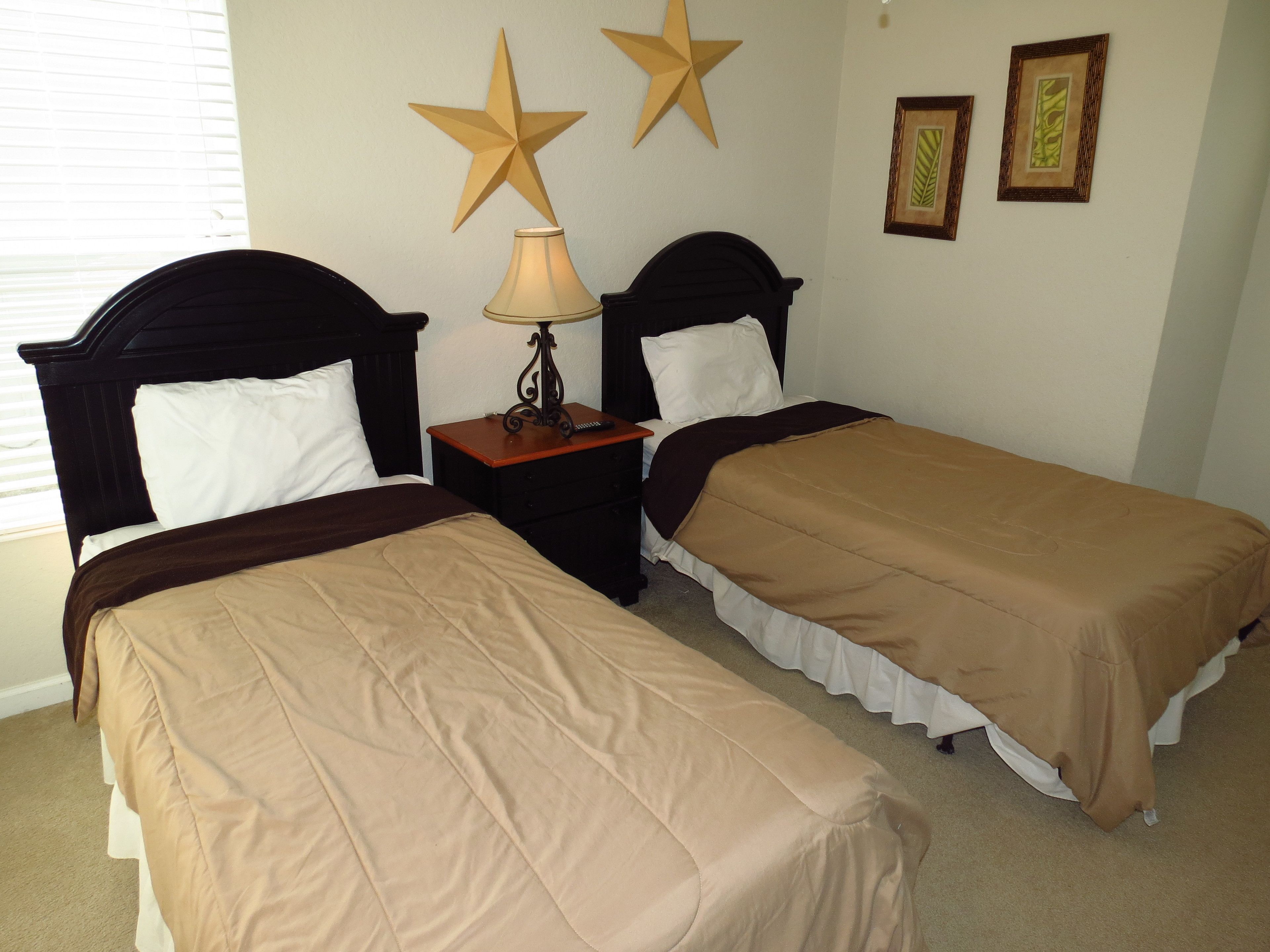 Una habitación con dos camas, una mesita de noche, una lámpara y detalles decorativos en las paredes, incluyendo estrellas y cuadros enmarcados.