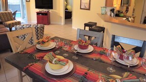 Un coin repas avec une table mise pour le repas, des chaises, un téléviseur et, au fond, un espace cuisine.