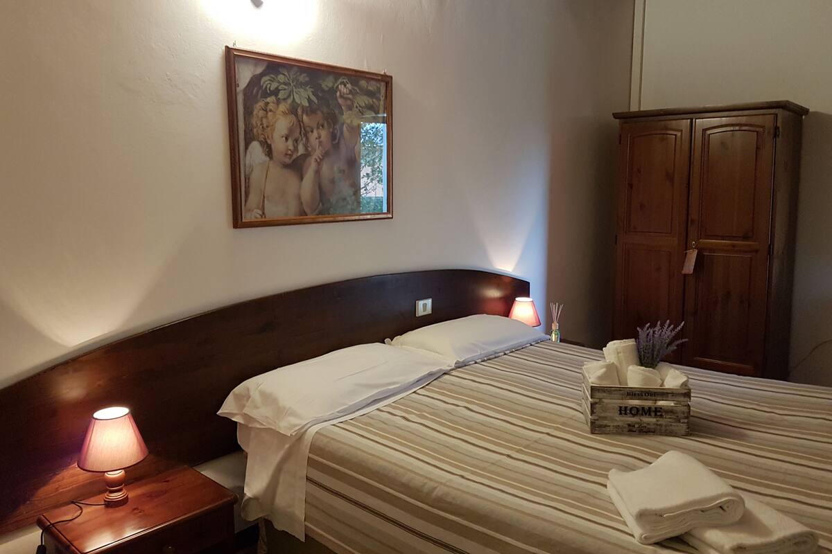 A neatly made bed with a striped bedspread, a wooden headboard, a bedside lamp, a framed picture on the wall, and a wooden cabinet.
