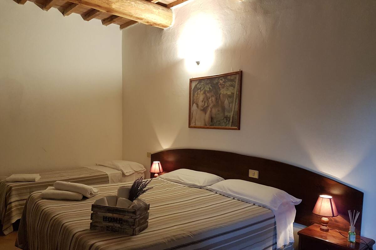 A hotel room with two beds, a wooden headboard, a nightstand with a lamp, a small table with a vase, and a painting on the wall.
